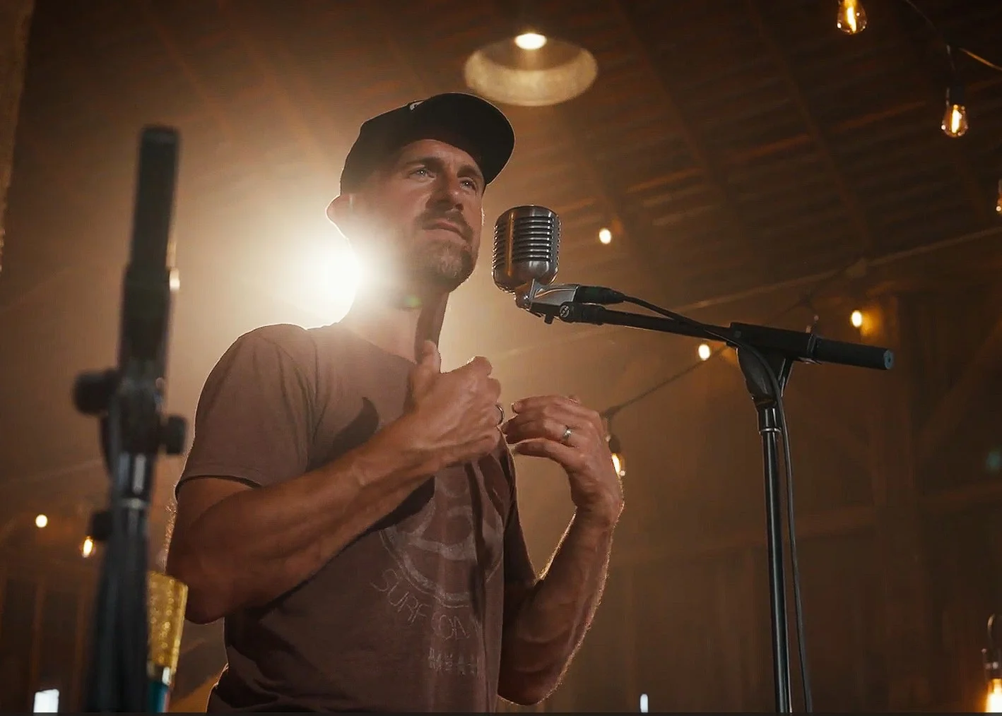 Drew Scholl speaking at a vintage microphone under warm barn lights